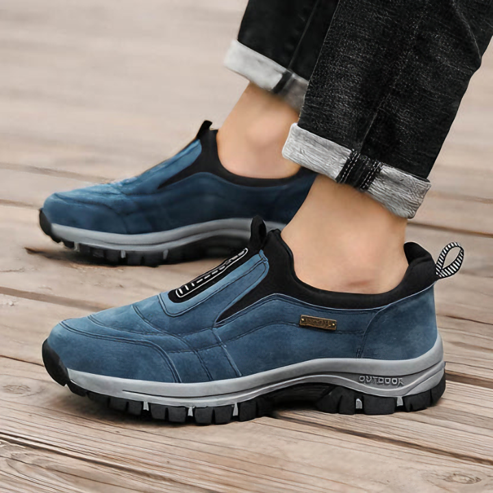 Blue suede slip-on hiking shoe worn with cuffed jeans on wood deck