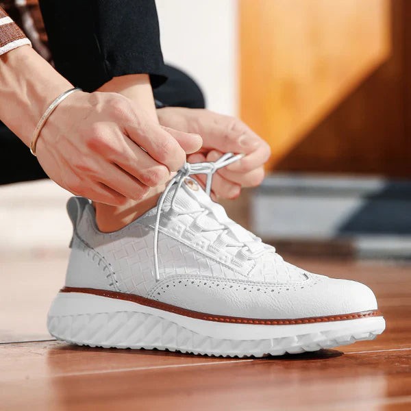 White leather sneaker being laced up showing woven panel and tan sole trim