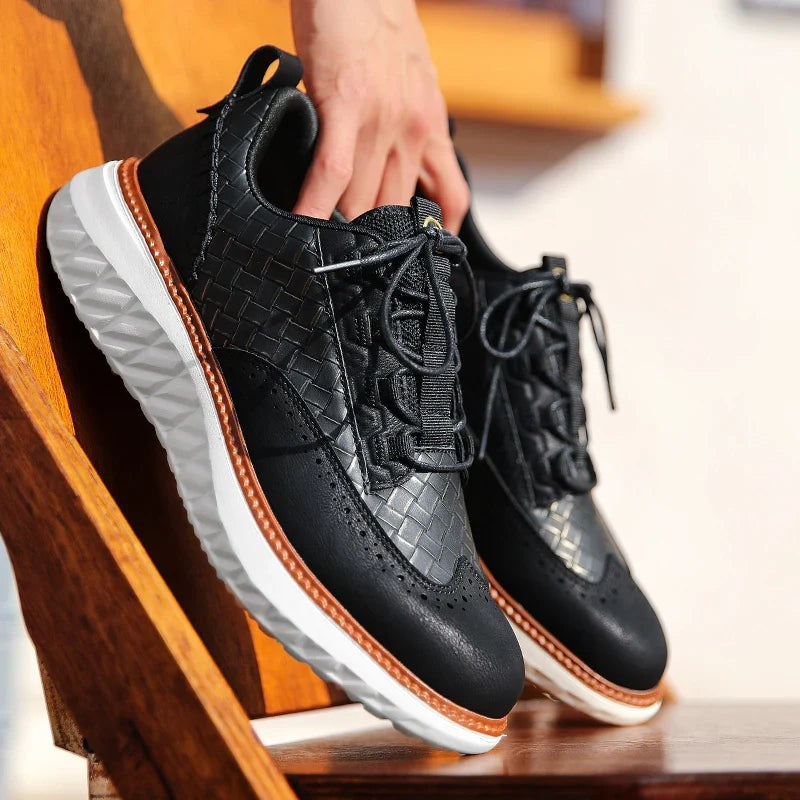 Black woven leather sneaker held by hand highlighting brogue perforations