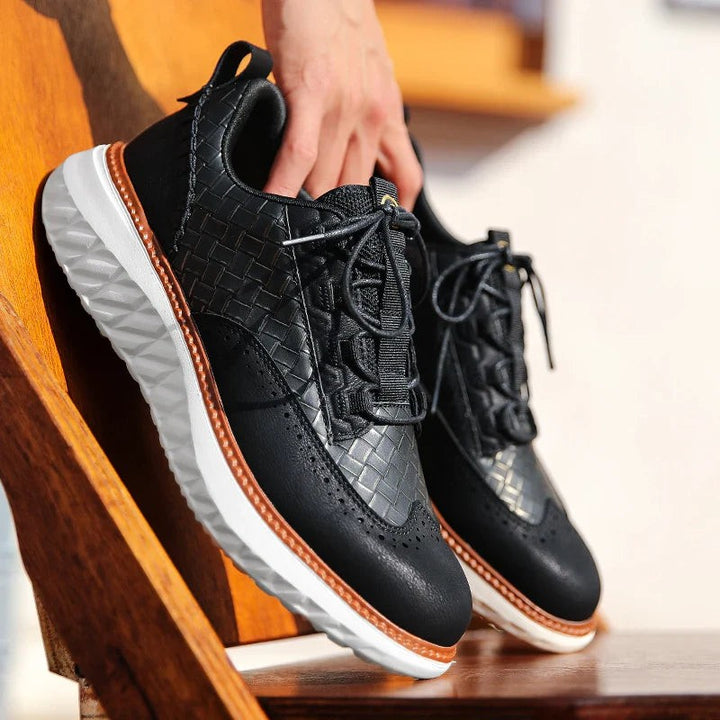 Black woven leather sneaker held by hand highlighting brogue perforations