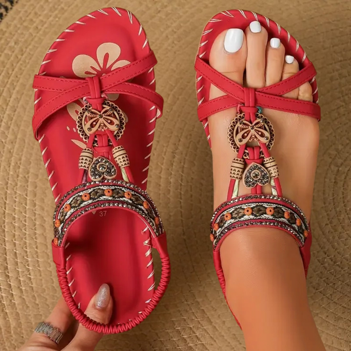 Red flat sandals featuring crisscross straps and beaded butterfly accent