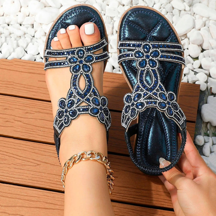 Navy blue rhinestone sandals with floral crystal straps worn outdoors on wood deck