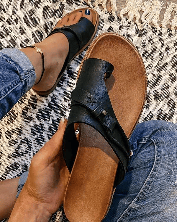 Black leather toe-ring sandal held in hand over leopard print rug