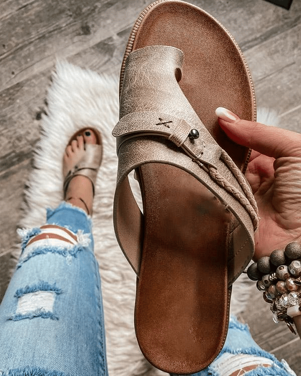 Metallic gold toe-ring sandal held in hand beside ripped denim jeans