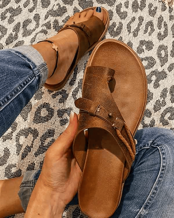Brown leather toe-ring slide sandal held in hand on leopard print mat