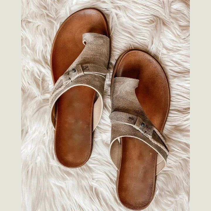 Pair of taupe toe-ring flat sandals with buckle strap on faux fur rug