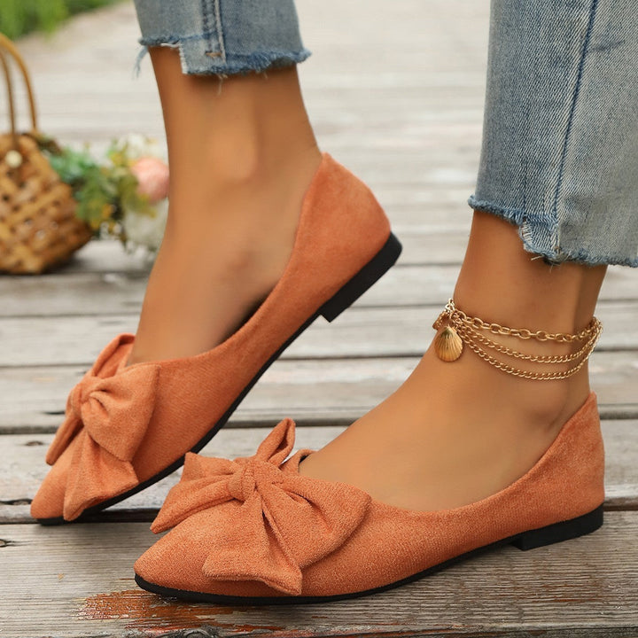 Orange suede pointed-toe ballet flats with bow detail worn on ankle chain
