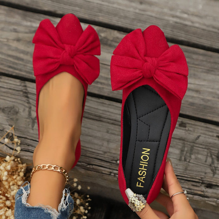 Red suede ballet flats featuring oversized bow accent, held by hand