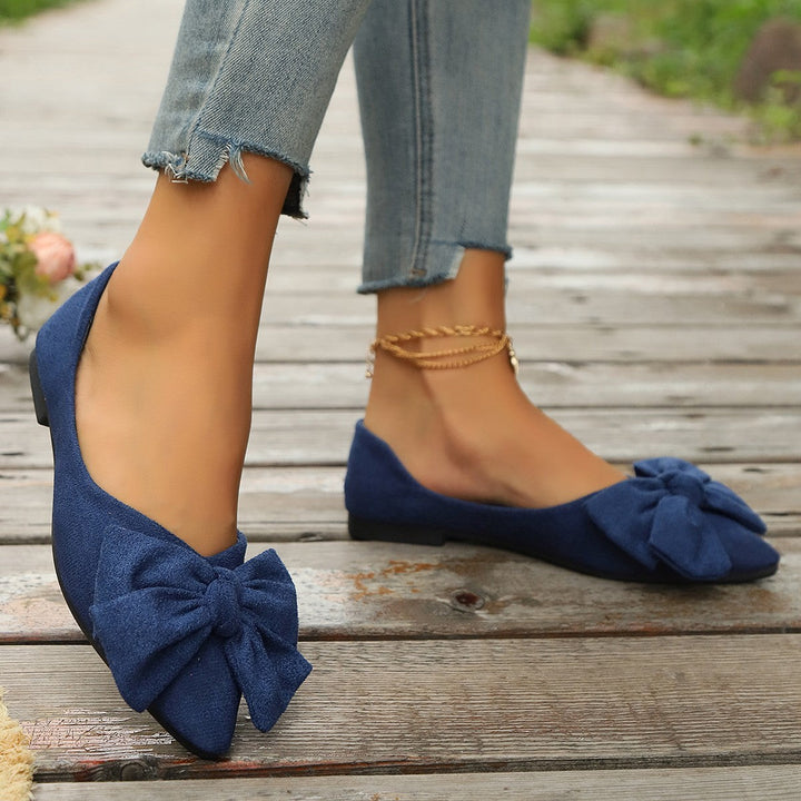 Navy suede bow-detail flats shown from side profile with ankle chain