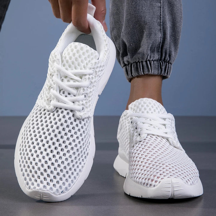 Close-up of white mesh sneakers held by hand showing lace detail