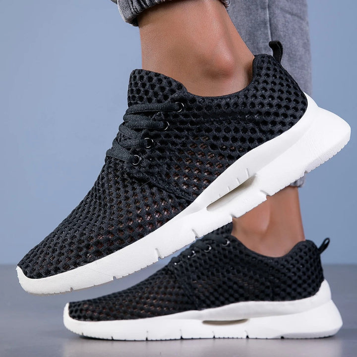 Black mesh sneakers with white sole worn on foot, side angle