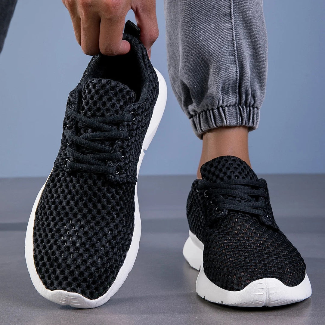 Black mesh sneakers held in hand highlighting lace-up closure