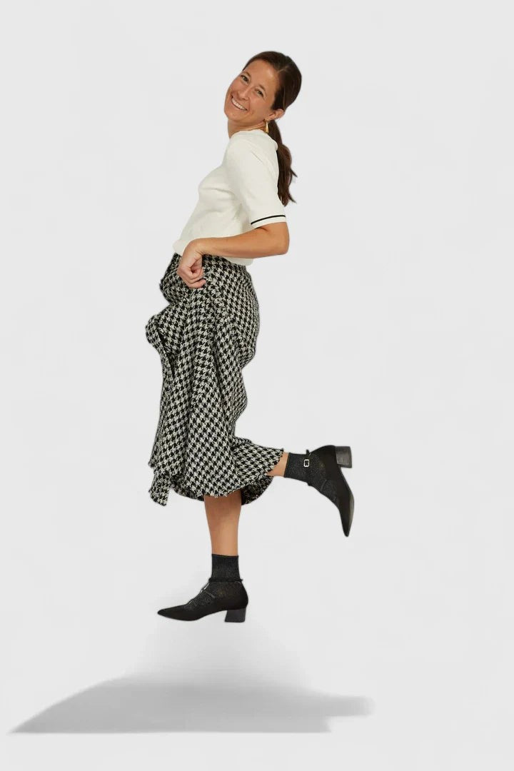 woman jumping in houndstooth midi skirt and black block-heel booties