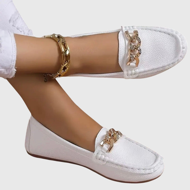 White leather loafers with rhinestone chain buckle and gold anklet accent