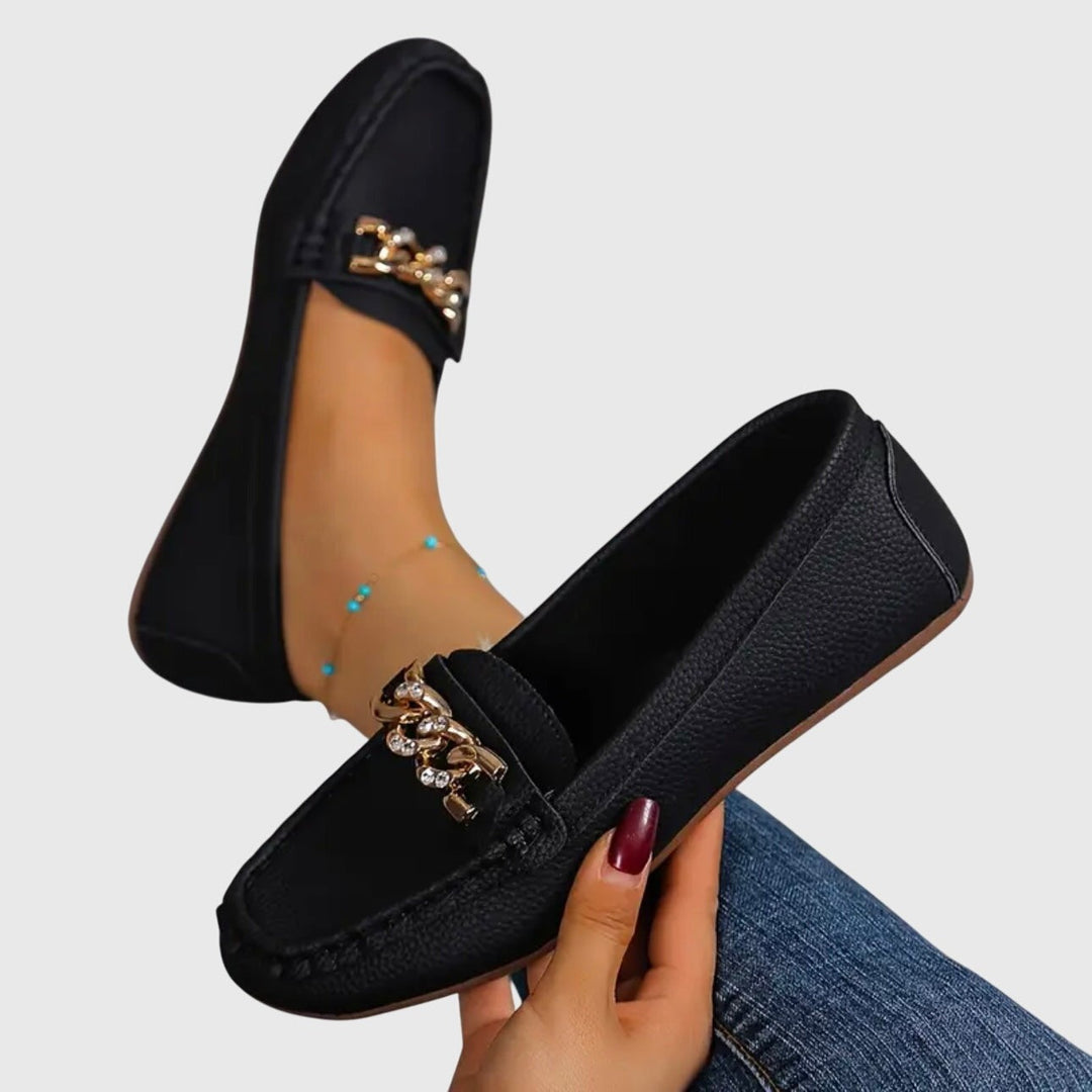 Black leather loafer held by hand, showing rhinestone chain buckle detail