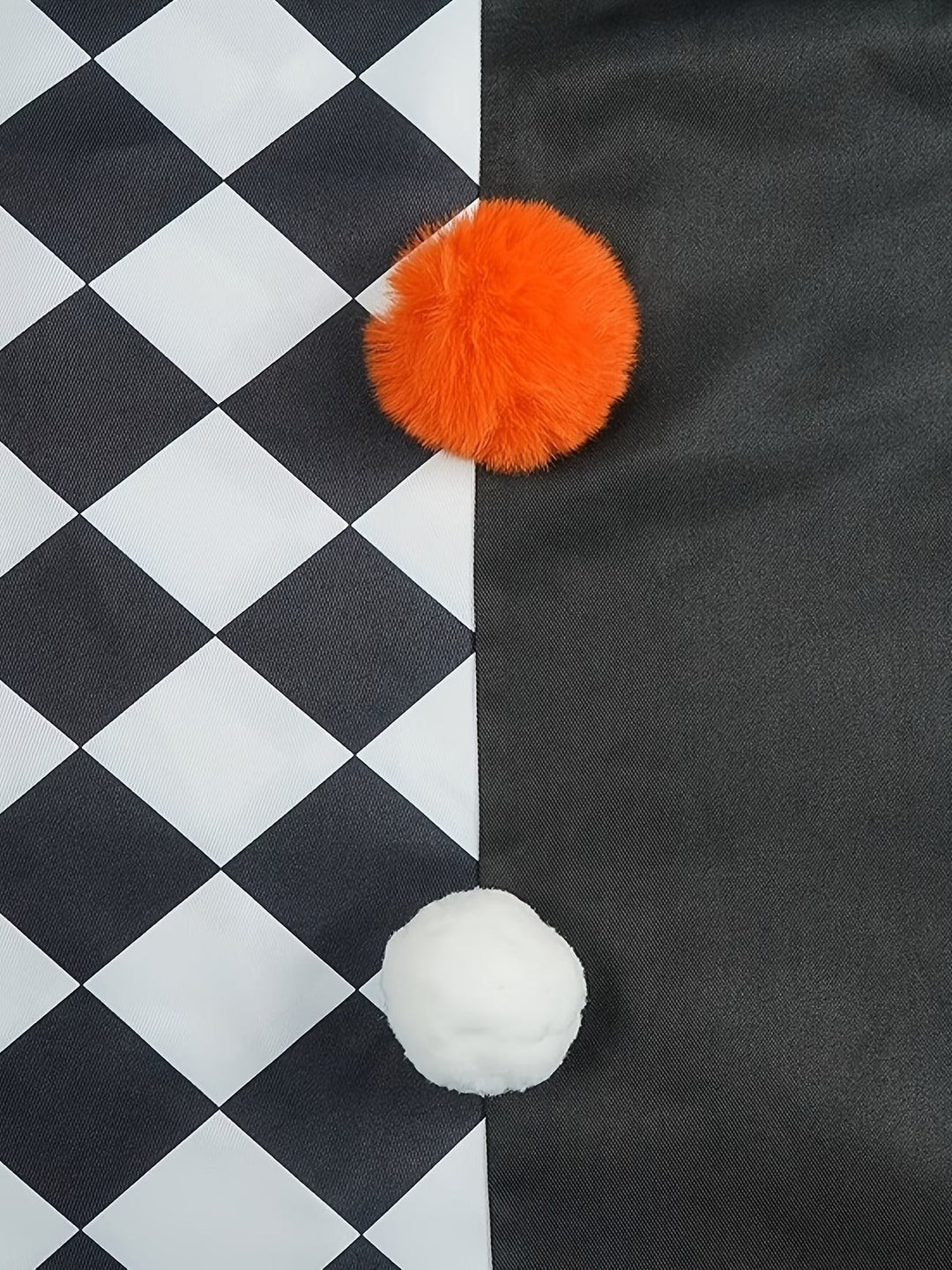 close-up of orange and white pom-pom accents on checkerboard cape fabric