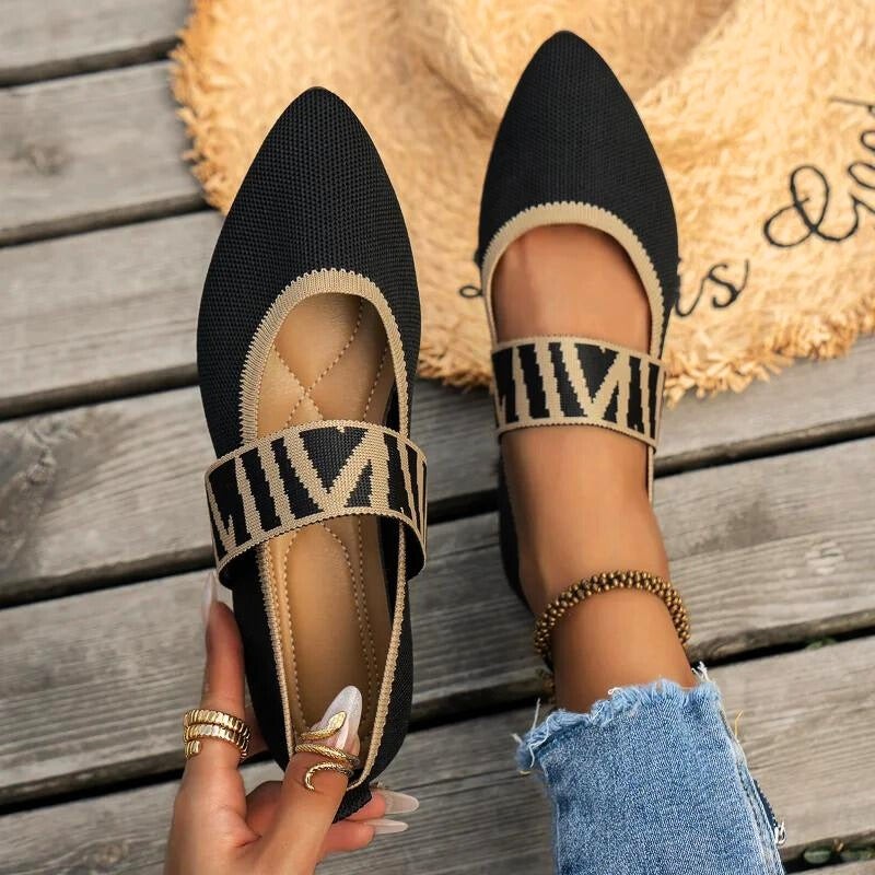 Black pointed-toe Mary Jane flats with gold striped strap, worn on foot