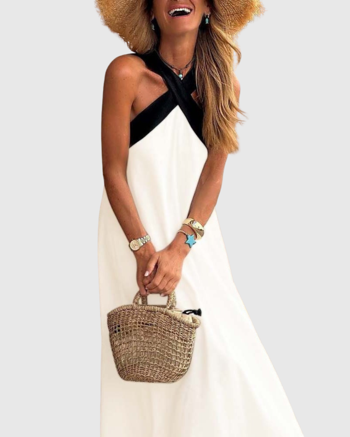 White maxi dress with black crisscross halter neckline and straw tote