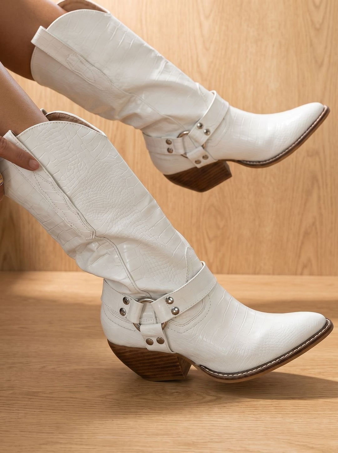 White croc-textured knee-high western boots with buckled harness strap and block heel