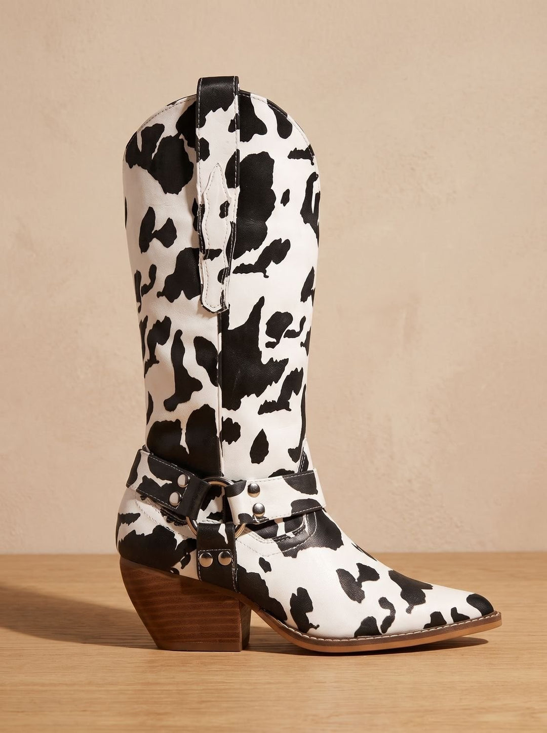 Black and white cow-print pointed-toe cowboy boot with harness buckle detail, side view