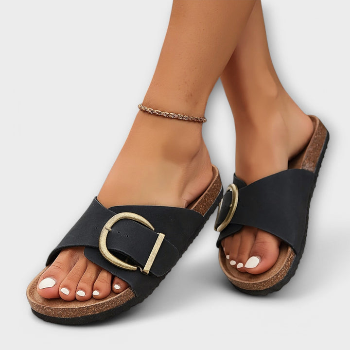 Black leather slide sandals with oversized gold buckle and cork footbed