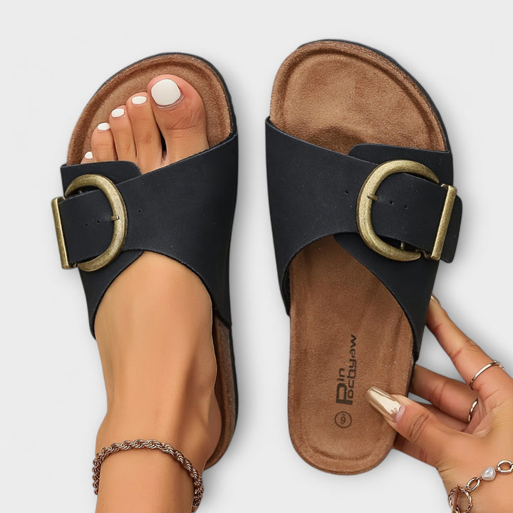 Top view of black slide sandals featuring chunky brass buckle detail