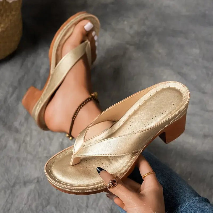 Gold thong sandal held in hand showing perforated insole and heel detail
