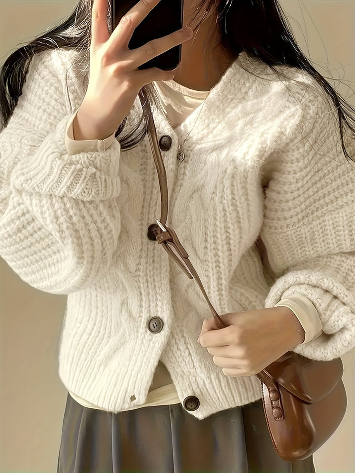 Close-up of cream chunky knit cardigan with dark buttons and cable-knit texture