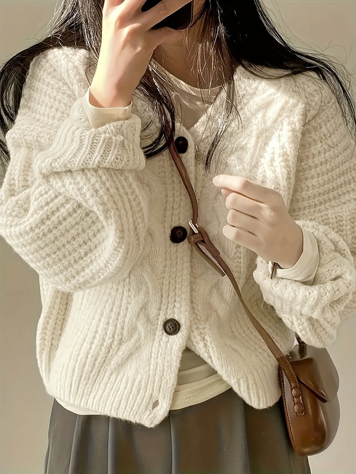 Cosy cream cable-knit cardigan paired with a pleated skirt and tan leather bag