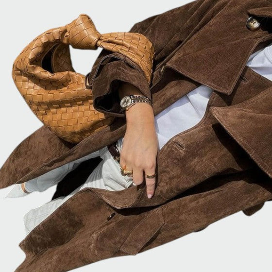 Close-up of brown suede trench coat sleeve with woven leather tote bag