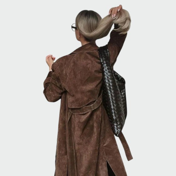 Back view of belted brown suede trench coat paired with a woven shoulder bag