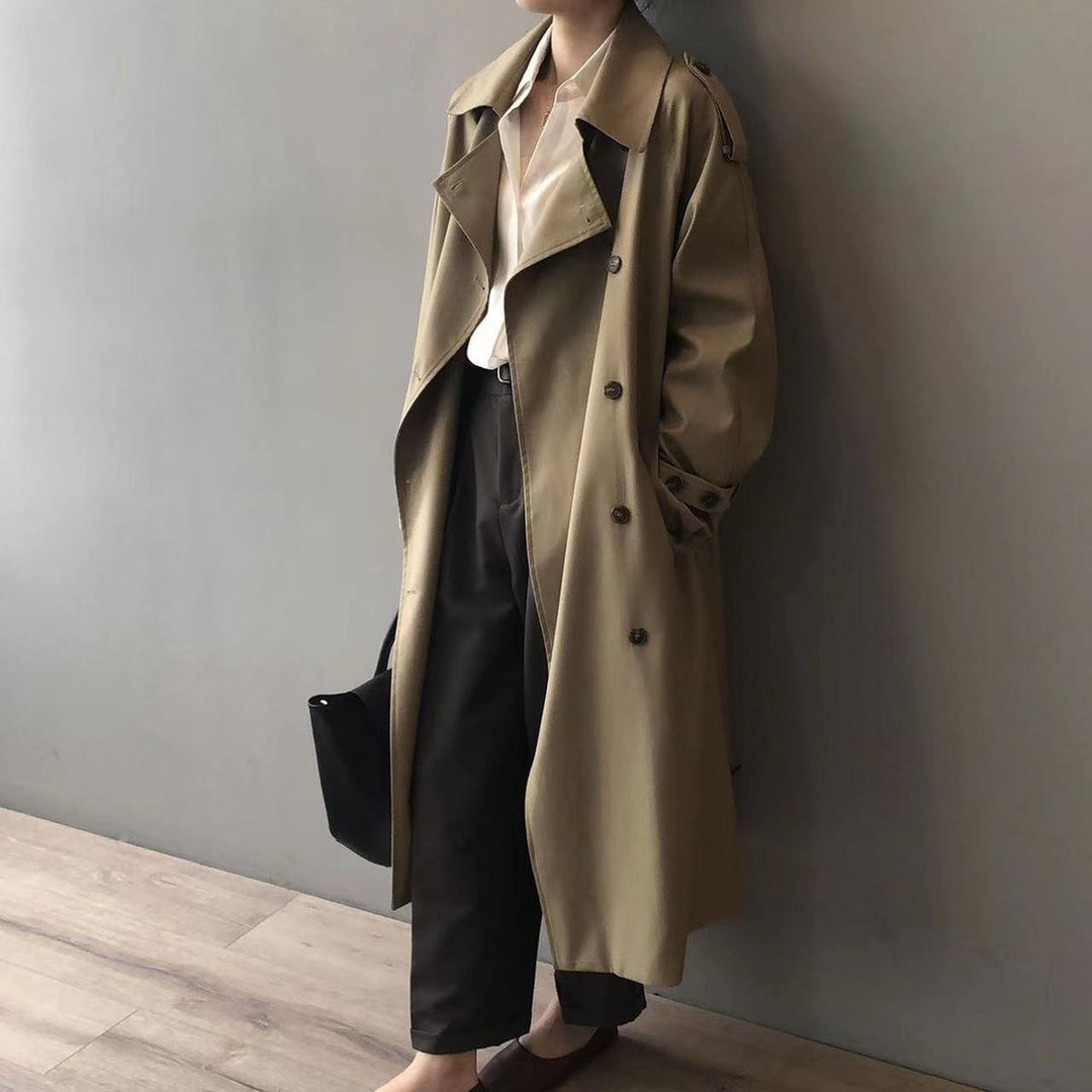 Khaki trench coat with button detailing and roomy sleeves, styled against a wall