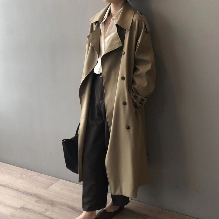 Khaki trench coat with button detailing and roomy sleeves, styled against a wall