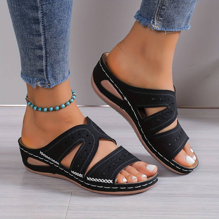 Black wedge sandals featuring crisscross stitching and embroidered open-toe straps