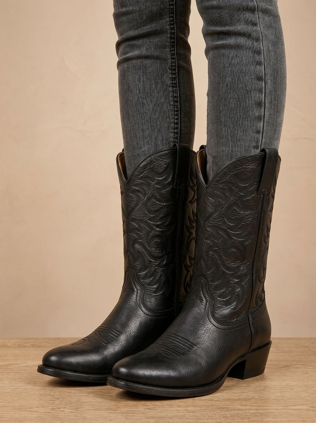 Black leather mid-calf cowboy boots with tonal stitched embroidery, worn with skinny jeans