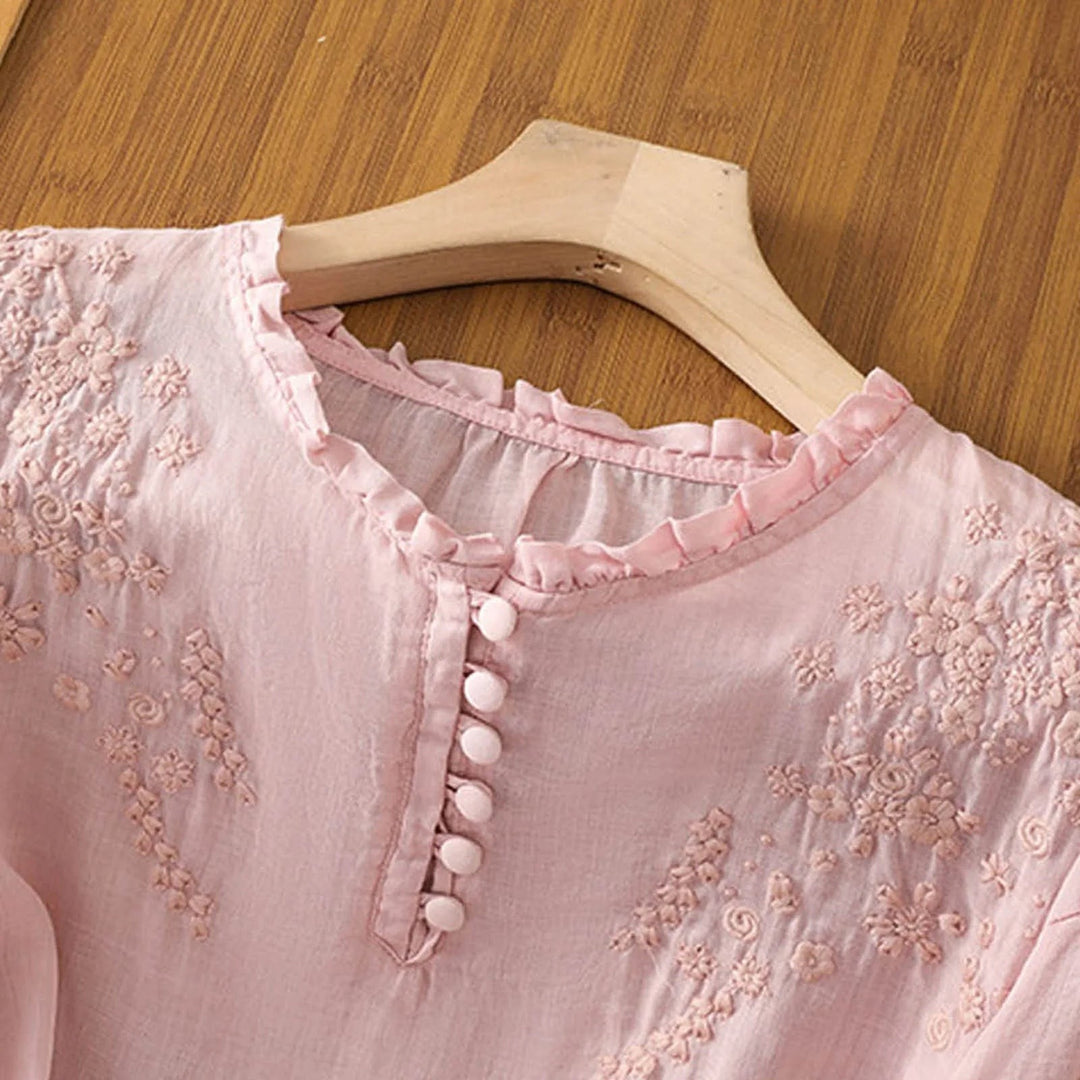 close-up of pink blouse ruffled neckline with floral embroidery and buttons