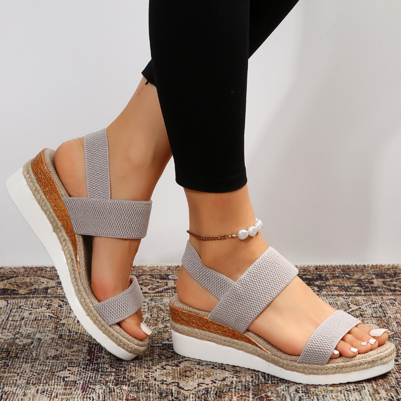 Gray crisscross wedge sandal with espadrille platform worn on patterned rug