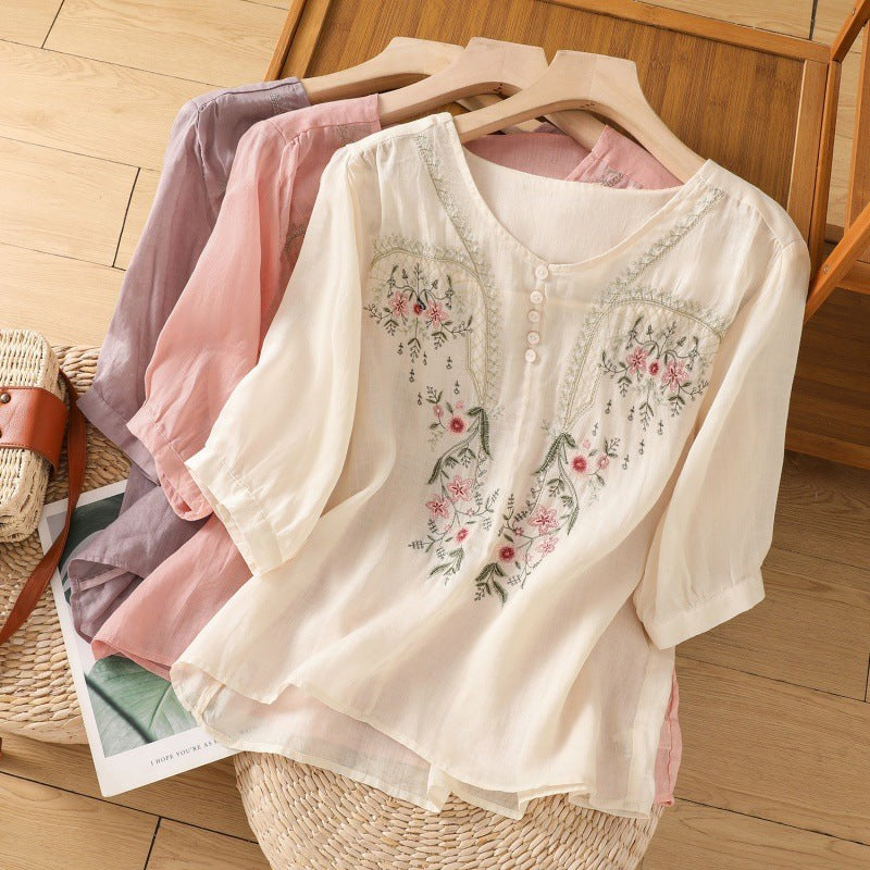 Three floral embroidered linen blouses in cream, pink, and mauve on hangers