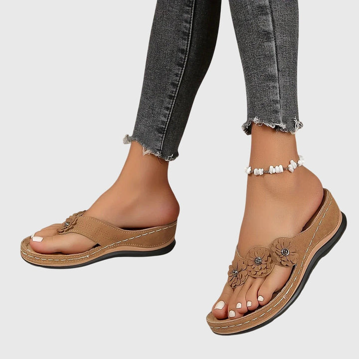 Tan floral wedge flip-flops worn on foot with ankle bracelet