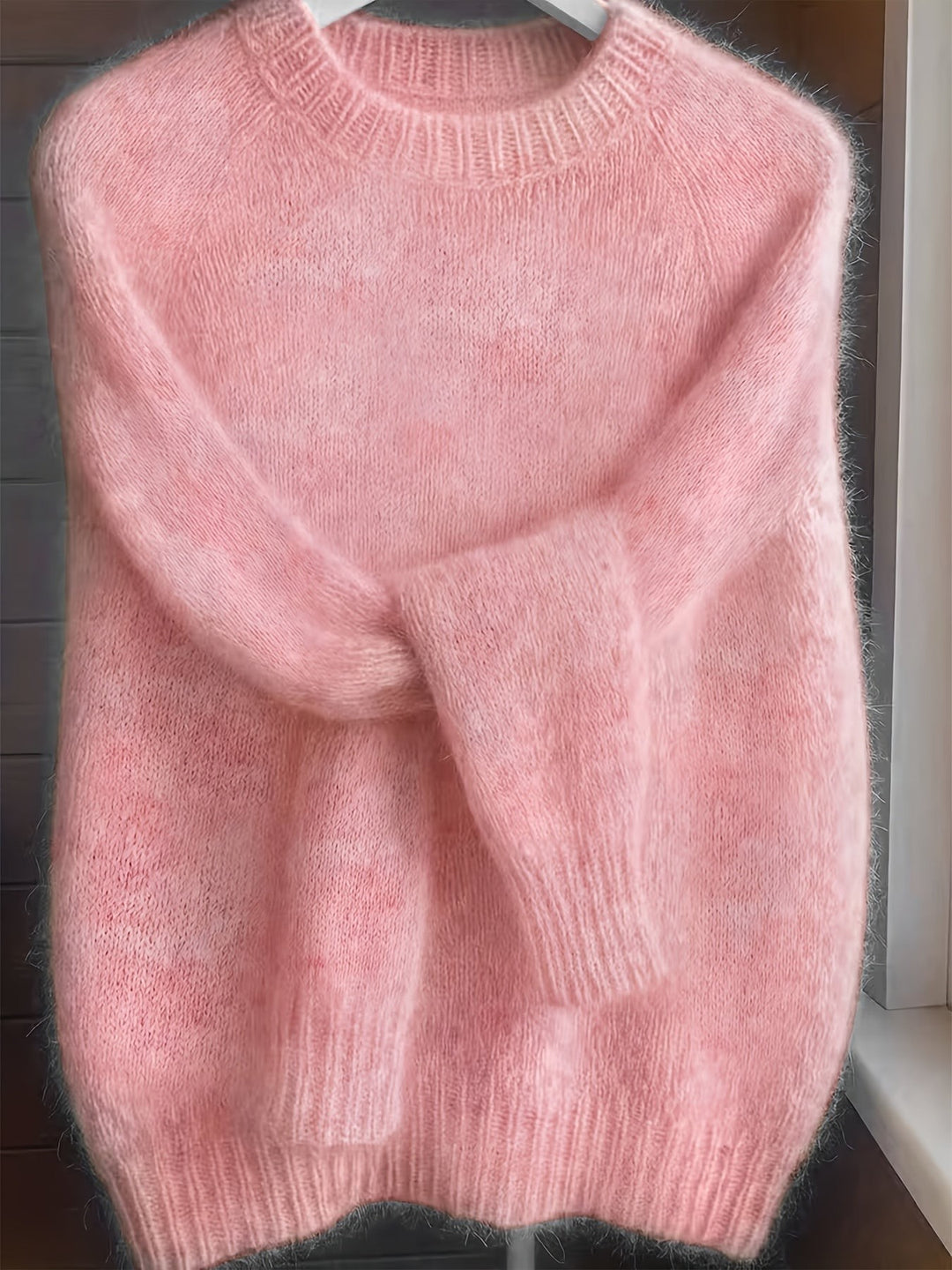 Pink fluffy knit jumper with ribbed crew neckline on a hanger