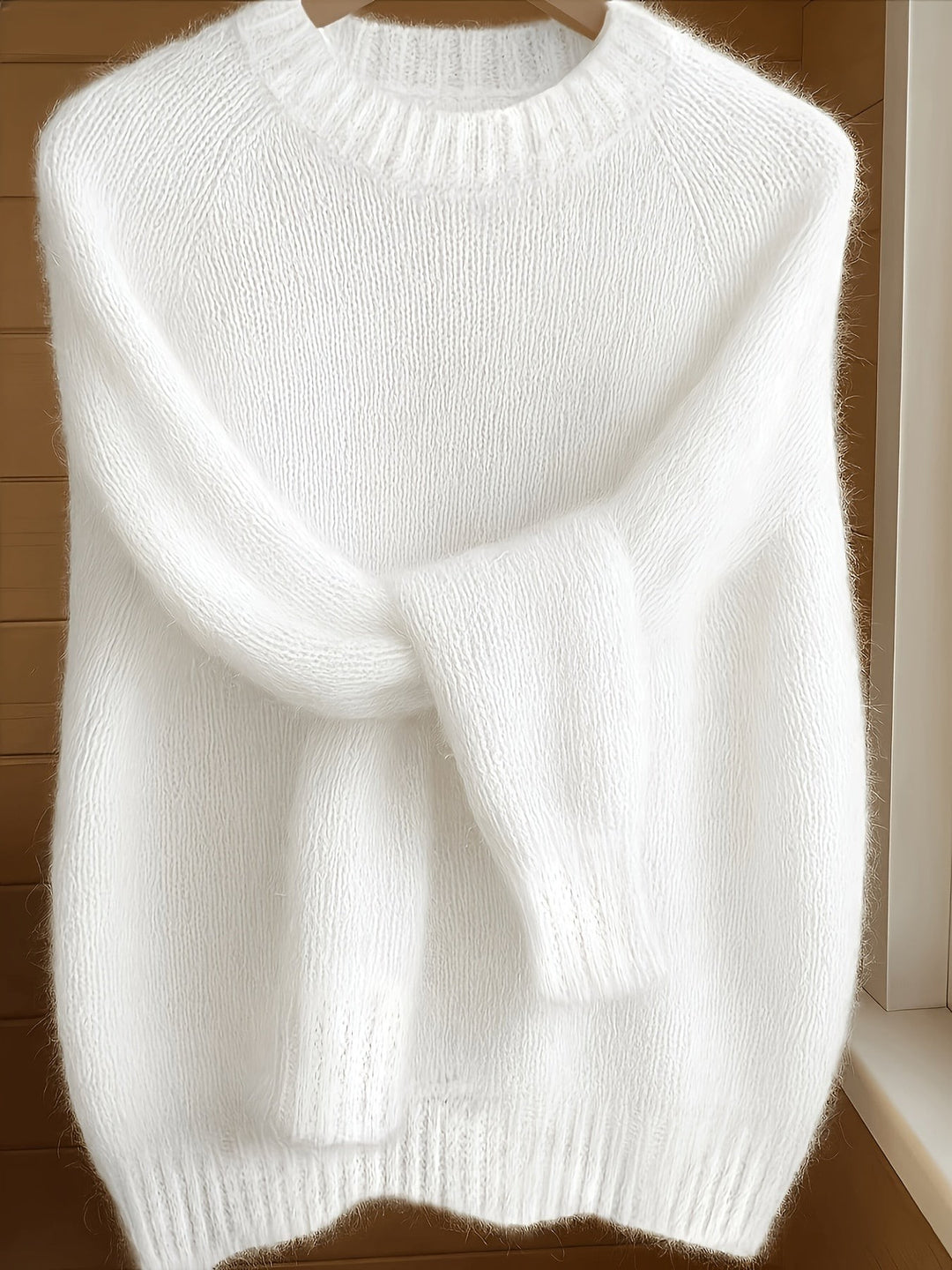 White fluffy knit jumper with ribbed collar hanging against a wooden door