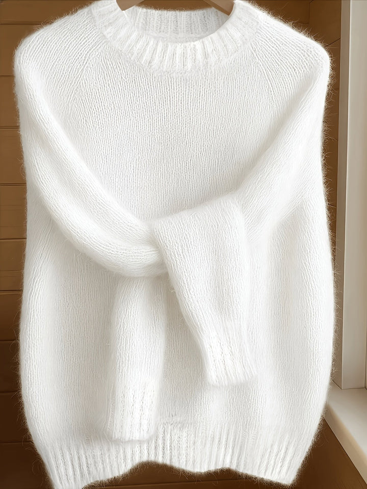 White fluffy knit jumper with ribbed collar hanging against a wooden door