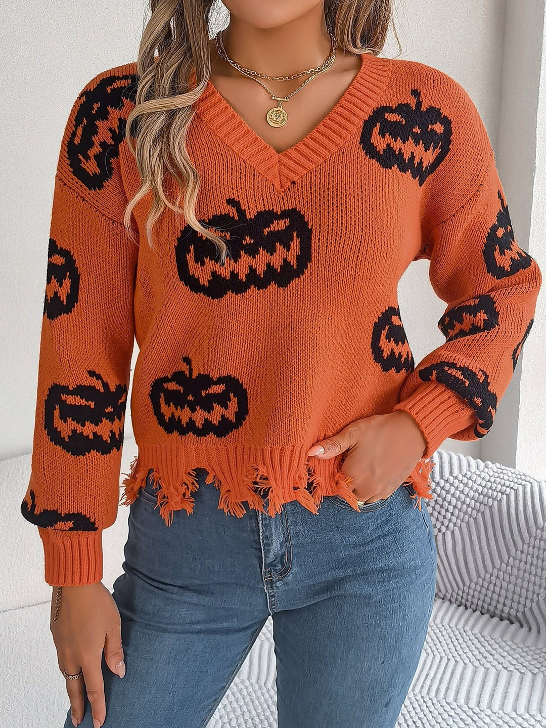 Orange V-neck sweater with black jack-o'-lantern print and frayed hem