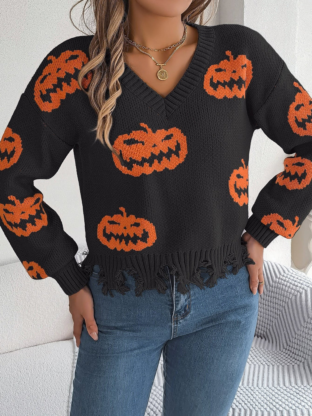 Black knit sweater featuring orange pumpkin print and frayed trim