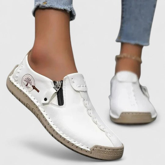 White leather slip-on sneakers featuring side zipper and hand-stitched trim