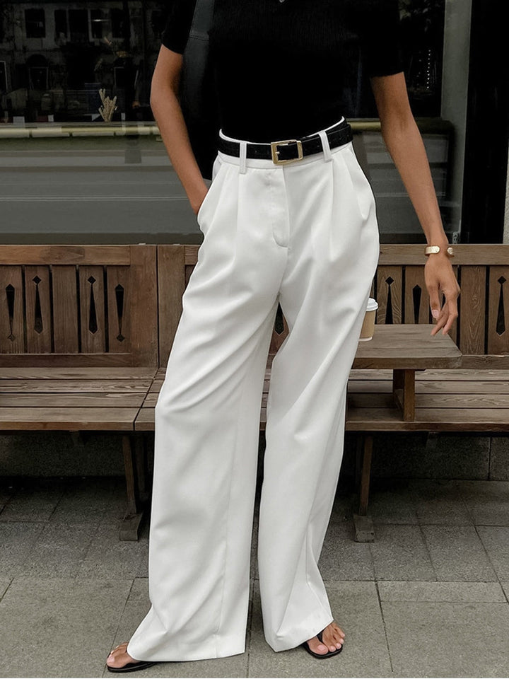 Pleated white wide-leg pants paired with black polo and leather belt