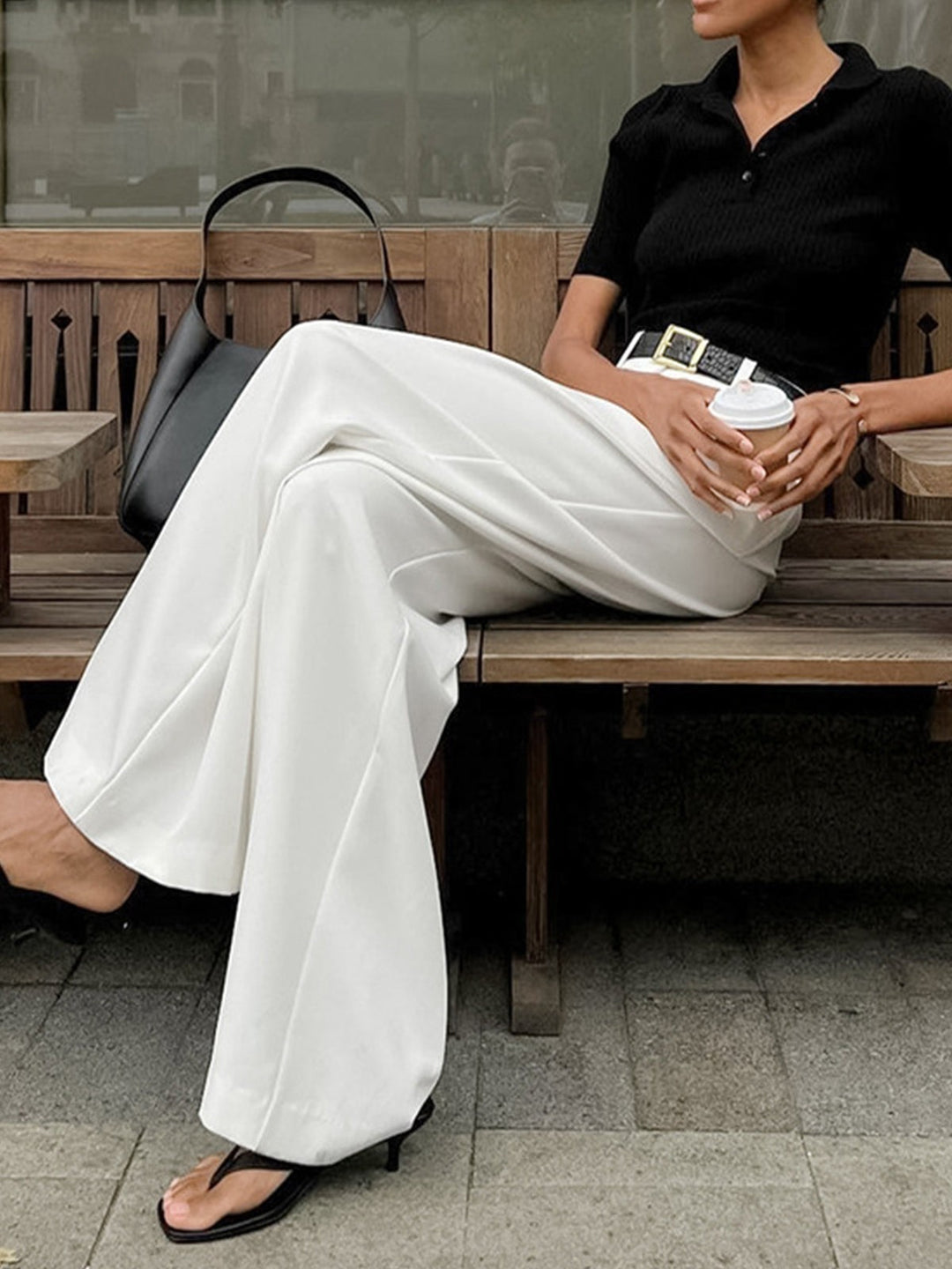 Woman seated wearing white wide-leg trousers with black bag and heels