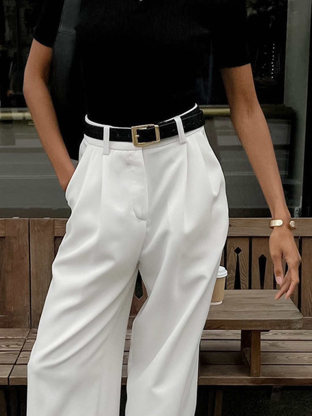 Close-up of white pleated trousers with black belt and gold buckle