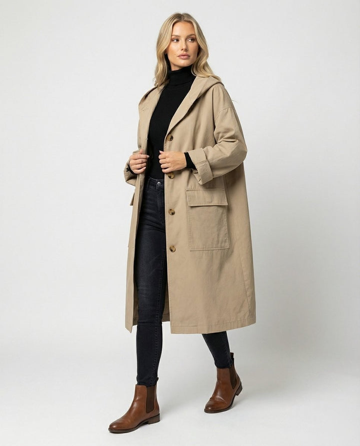 Model wears beige hooded trench coat with black roll-neck jumper and jeans
