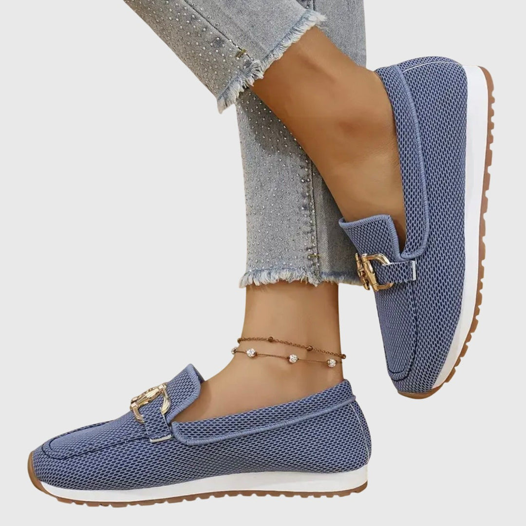 Gray knit loafers with gold buckle detail, held by hand